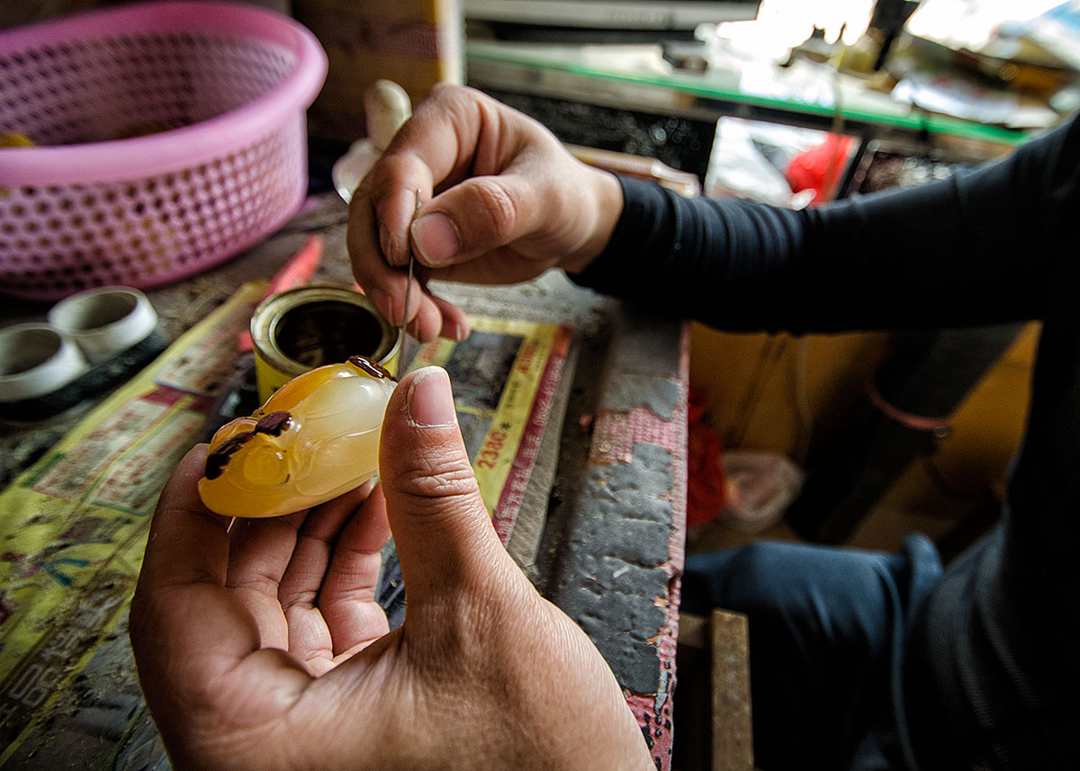 Applying a reddish varnish to the surface of a jade-like material in a workshop in Ruili's jade market. Following the treatment, which probably involves firing in an oven, the treated portions assume a reddish color that simulates the natural oxidation staining on the surface of jade boulders. Lotus Gemology on jade, nephrite, jade treatments.