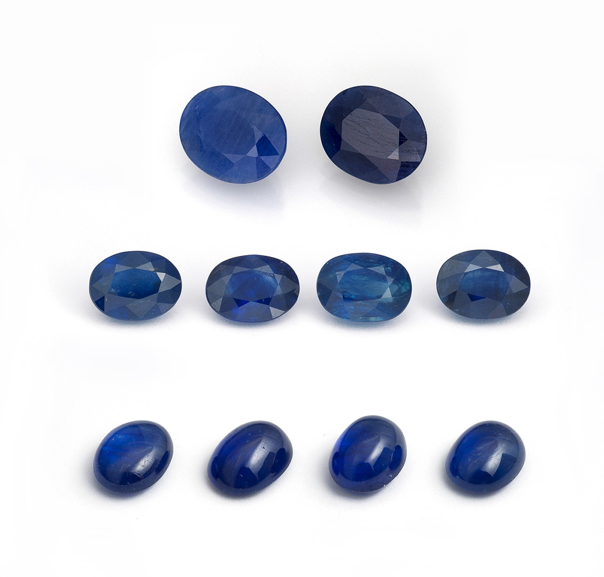 Figure 2. Two first-generation cobalt-doped glass-filled sapphires (top row; 3.49 & 3.37 ct), along with eight latest-generation cobalt-doped glass-filled sapphires ranging from 1.50–2.25 ct each that were tested as part of this study. Note the far lower clarity of the first-generation stones. (Photo: Lotus Gemology's Wimon Manorotkul).