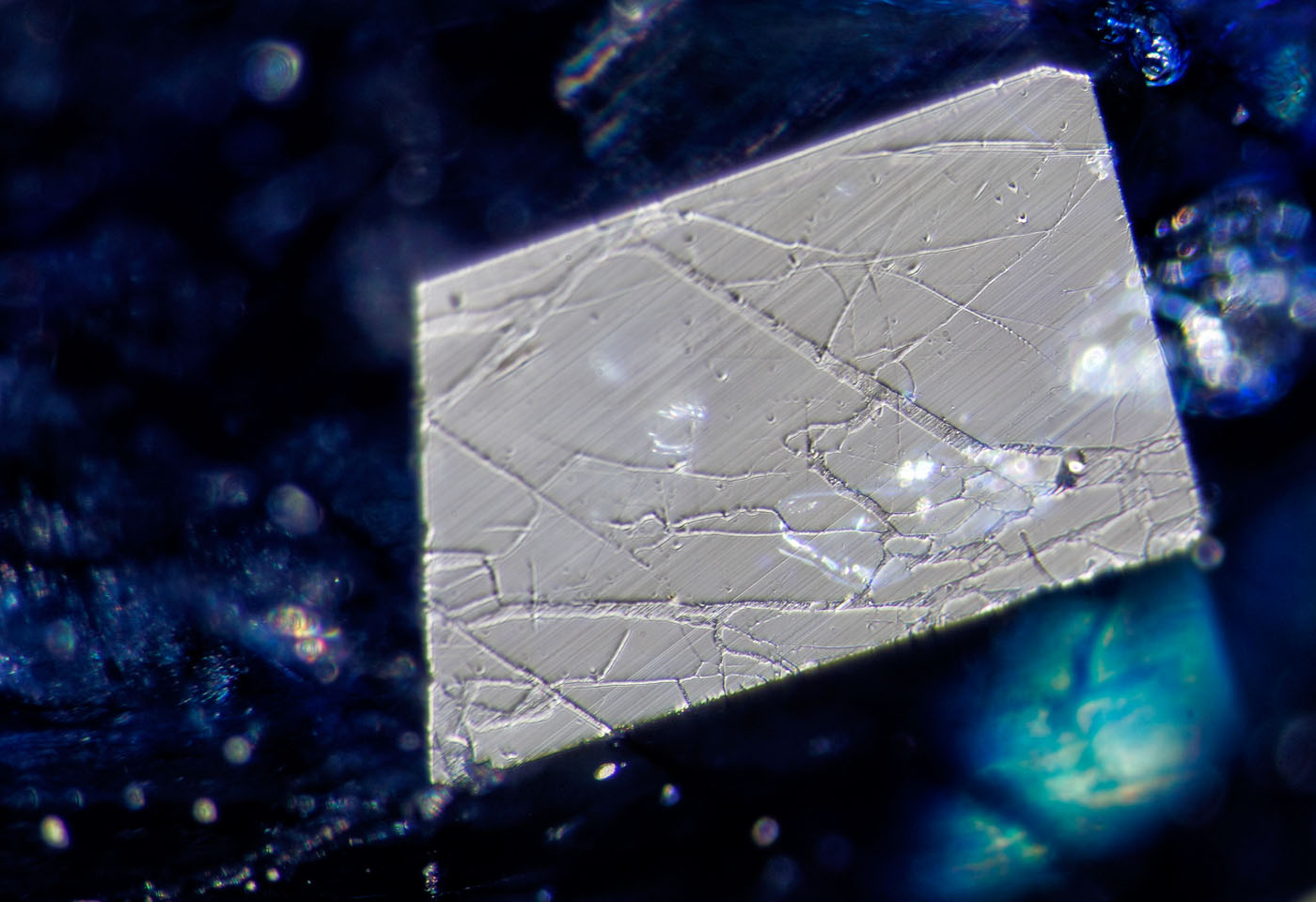 Figure 10. A small facet viewed in reflected light reveals a network of fissures filled with glass. The low hardness of the glass shows serious undercutting compared with the surrounding sapphire. Surface-incident fiber-optic illumination. (Photo: Wimon Manorotkul, Lotus Gemology).