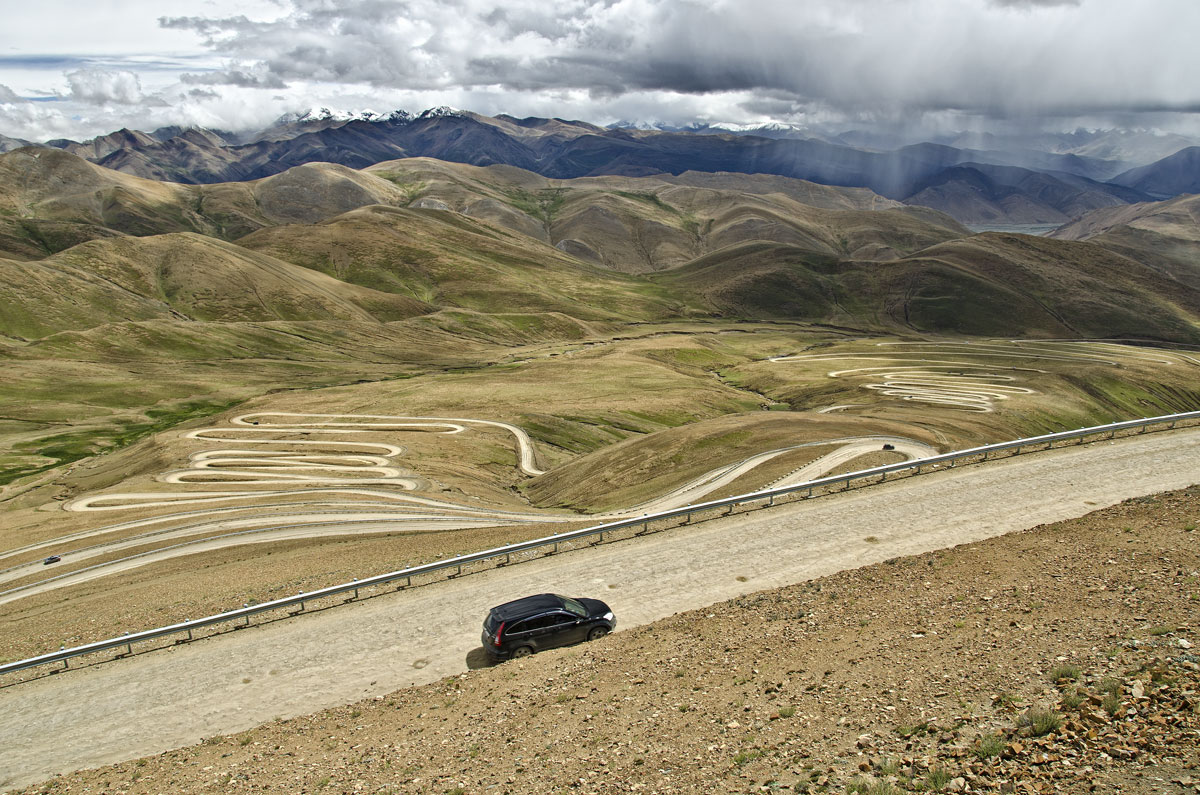 Twistin' an' turnin' in Tibet At 8848 m (29,028 ft), Mount Everest lies in a region that contains many of the world's highest peaks. The northern base camp is eight hours' drive west of Shigatse, with the road winding over two major passes. In this photo, taken atop Pang La (5050 m; 16,568 ft), Everest lies behind the clouds in the distance. Photo: Richard W. Hughes