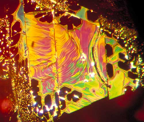 Figure 4.  …equals internal symmetry Secondary fluid inclusions (healed fractures, or ‘fingerprints’) often display the symmetry of the underlying crystal structure in the healed areas. Above is shown a healed fracture in a Thai ruby which formed parallel to the basal pinacoid. As the c axis (3-fold symmetry) runs perpendicular to this face, the healed (dark) areas display distorted hexagonal or triangular (60/120°) outlines. Vertical lines cutting through the fingerprint are repeated twinning striations. Photo © Richard W. Hughes